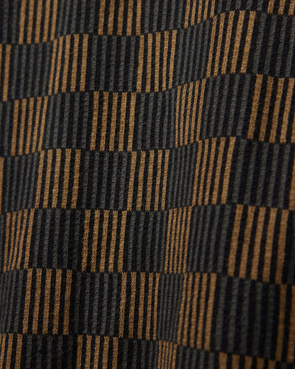 This close-up showcases The Sebastian Knit Polo in Onyx by Dandy Del Mar, featuring an Italian knit fabric with a checkered pattern of alternating black and brown stripes, creating an optical illusion.